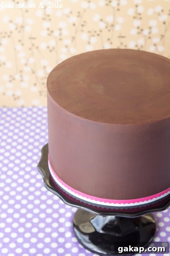 Perfect Ganache for Cakes: Step-by-Step Guide and Tips 9 Close up of the finished ganached cake on a black cake stand with a pink and white ribbon around the base.