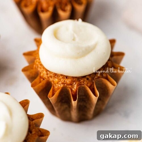 Super moist carrot cake cupcakes topped with cream cheese frosting on a white background.