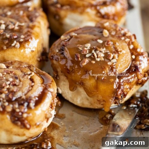 Sticky buns placed on a stainless steel baking sheet with a small knife placed next to them on a white background.