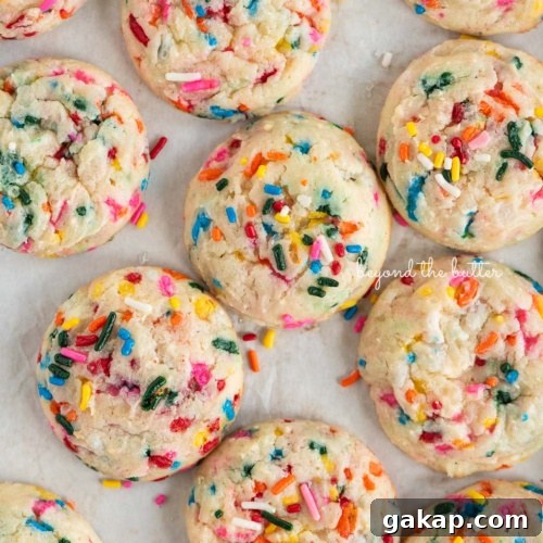 Funfetti butter cookies topped with sparkling sugar placed randomly on a white sheet of parchment paper.