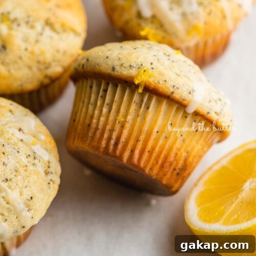 Randomly placed lemon poppy seed muffins on a parchment paper-lined baking sheet with half of a lemon.
