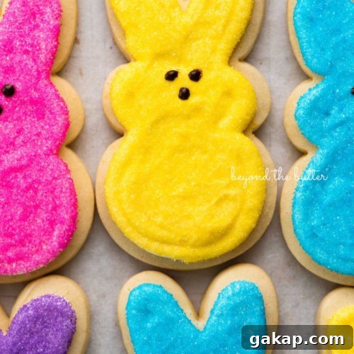 Easter bunny cut out sugar cookies topped with frosting and colors of pink, yellow, blue, and purple sanding sugars on a parchment paper lined baking sheet.