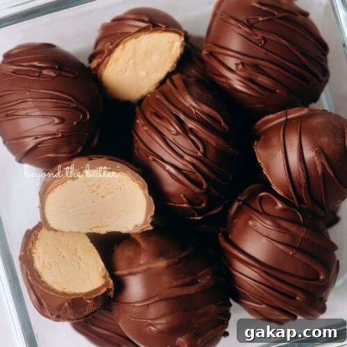 Chilled chocolate covered peanut butter eggs drizzled with more chocolate randomly placed in a glass container with two cut in half on white background.