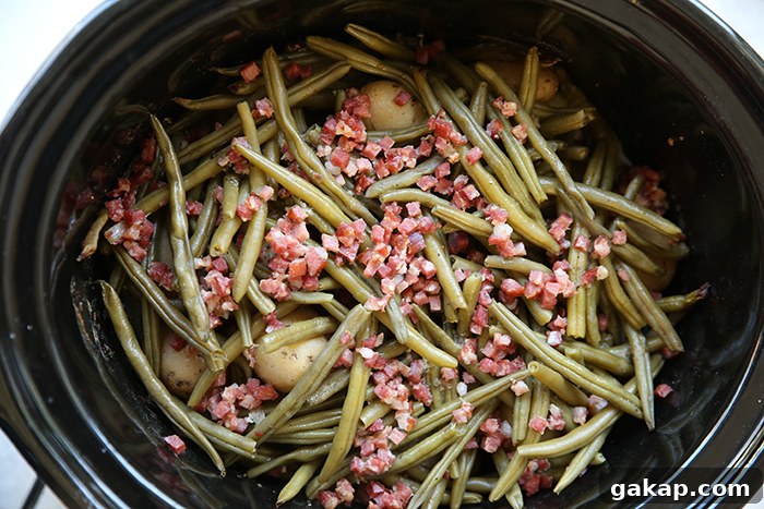 A slow cooker filled with baby potatoes, green beans, and cubed bacon pieces.