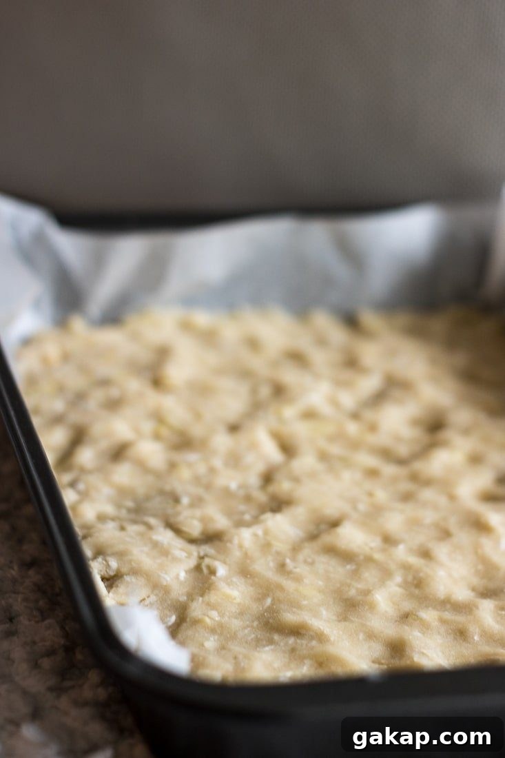 Almond Coconut Shortbread Bars Recipe with Crispy Coconut Crust 3 Dough spread on a rectangular sheet pan lined with parchment paper.