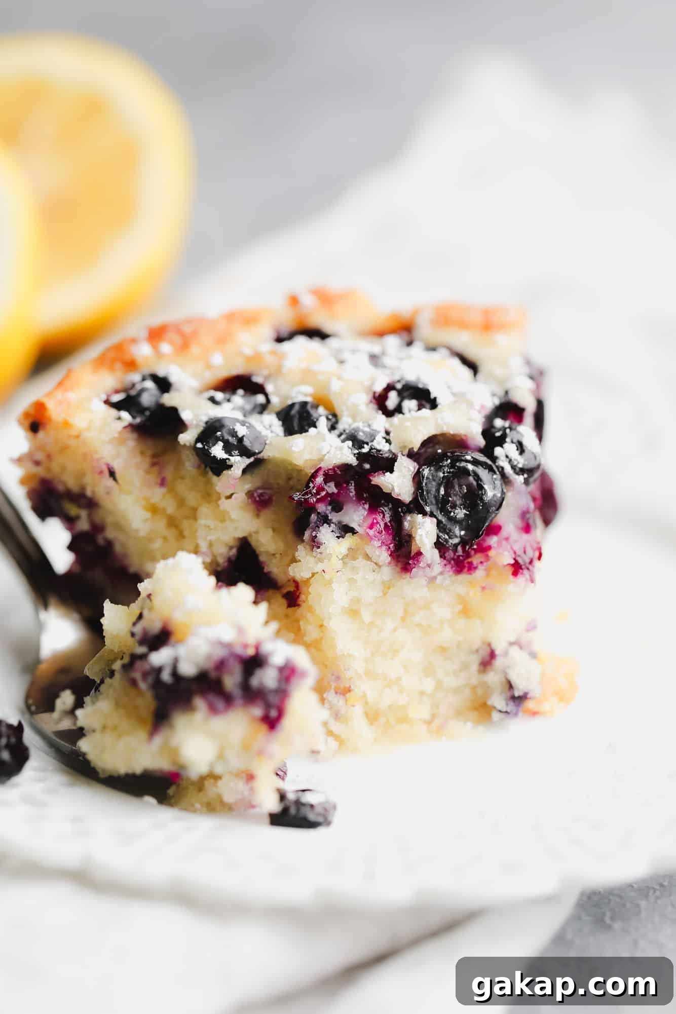 Moist Vegan Blueberry Layer Cake Recipe 3 close up on a slice of vegan blueberry cake with a bite missing on a white plate.