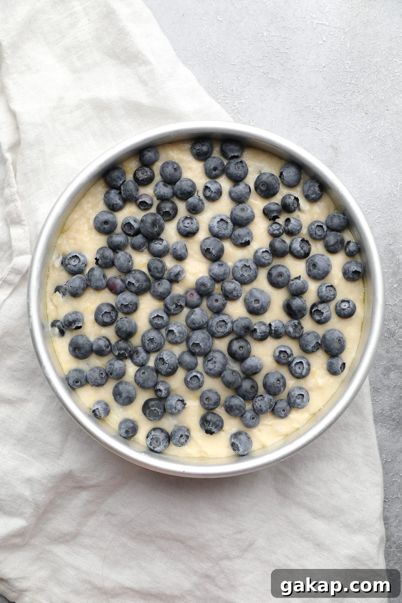 Moist Vegan Blueberry Layer Cake Recipe 4 blueberry cake batter with fresh blueberries on top in a round metal cake pan.