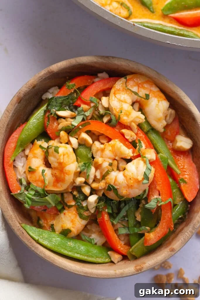 small wood bowl with brown rice and a shrimp curry with shrimp, bell pepper, snap peas, basil and peanuts