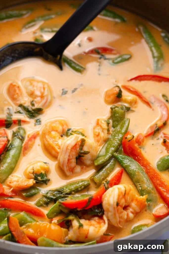 Close up view of a red Thai Prawn curry featuring a creamy coconut curry sauce, snap peas, bell pepper and shrimp.