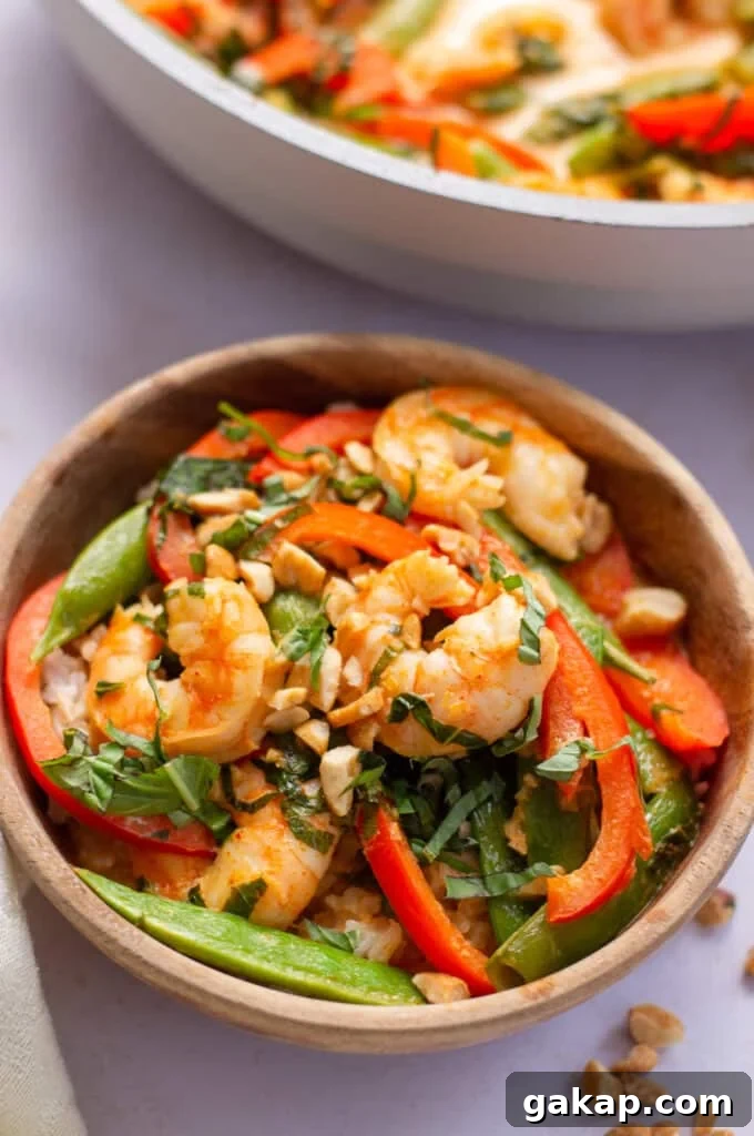 Wooden bowl containing Thai prawn curry- a coconut based curry sauce, shrimp, red bell pepper and snap peas. Topped off with fresh basil and chopped peanuts.