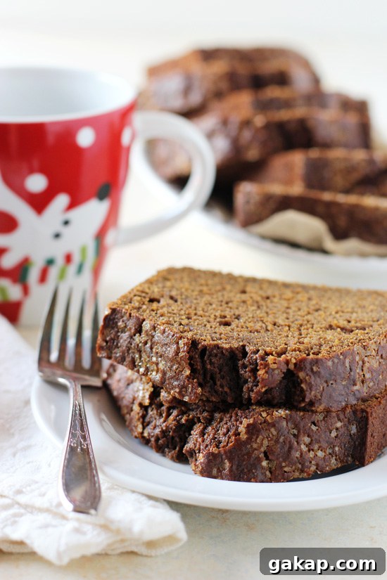 Two pieces of Healthy Maple Gingerbread Loaf on a plate with a cup of coffee in the background.