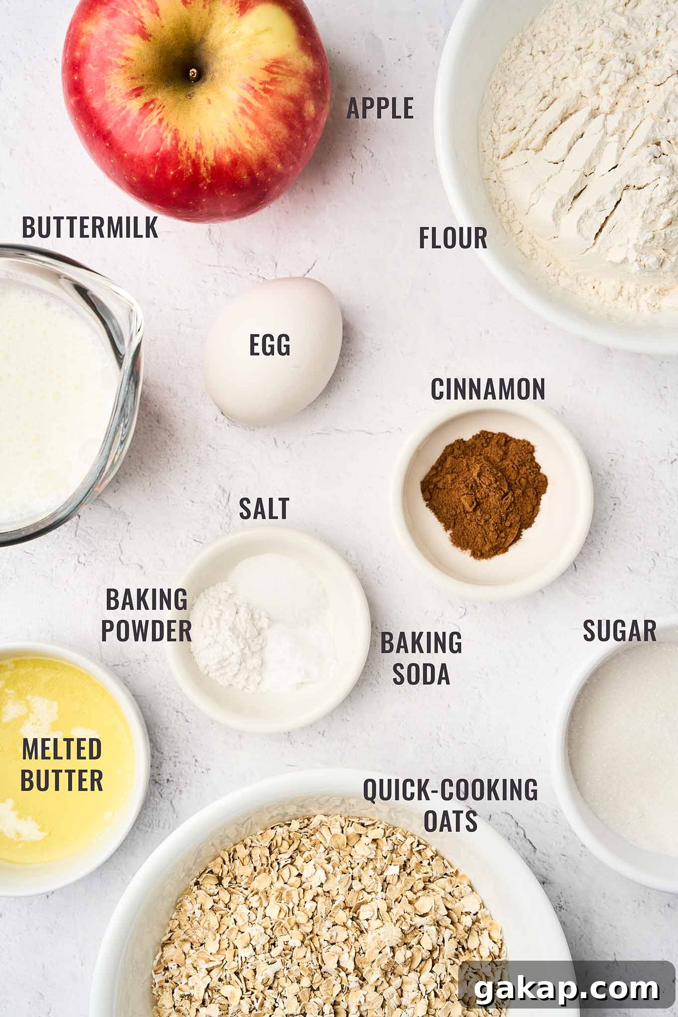 Buttermilk Apple Oat Muffins Recipe for Moist Breakfast 3 A labeled, overhead view of the ingredients needed to make apple cinnamon oatmeal muffins; flour, oats, sugar, cinnamon, egg, melted butter, buttermilk, apple, baking soda, powder, and salt.