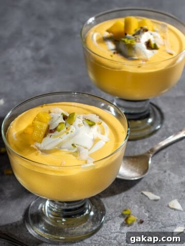 Two bowls of mango mousse in dessert cups with a swirl of cream and nuts.