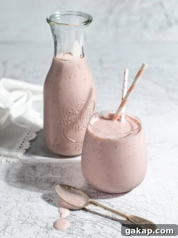 A glass and a carafe of strawberry lassi on a white background.