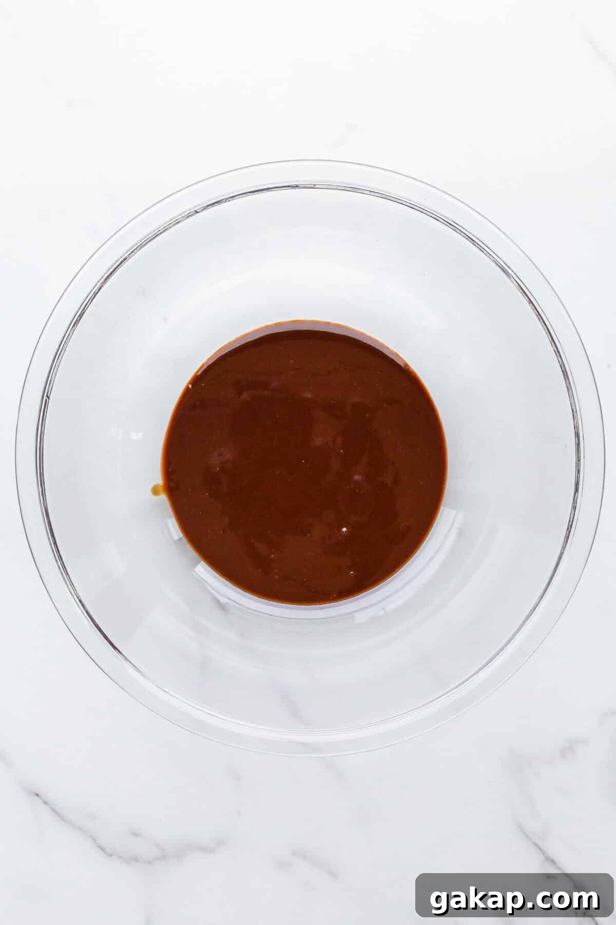 A glass bowl of melted chocolate and butter to make chocolate frosting.
