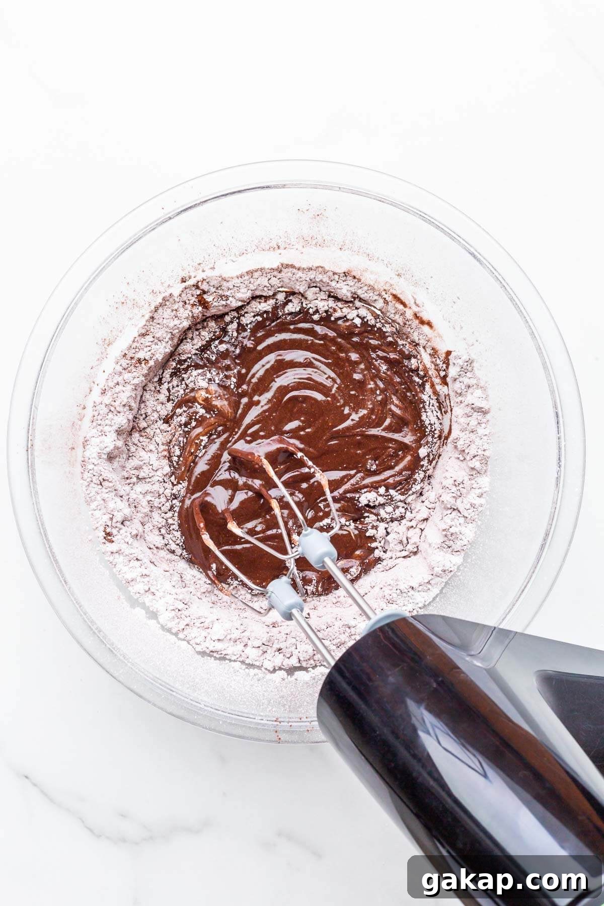 Beating ingredients in a glass bowl with an electric mixer to make chocolate fudge frosting.