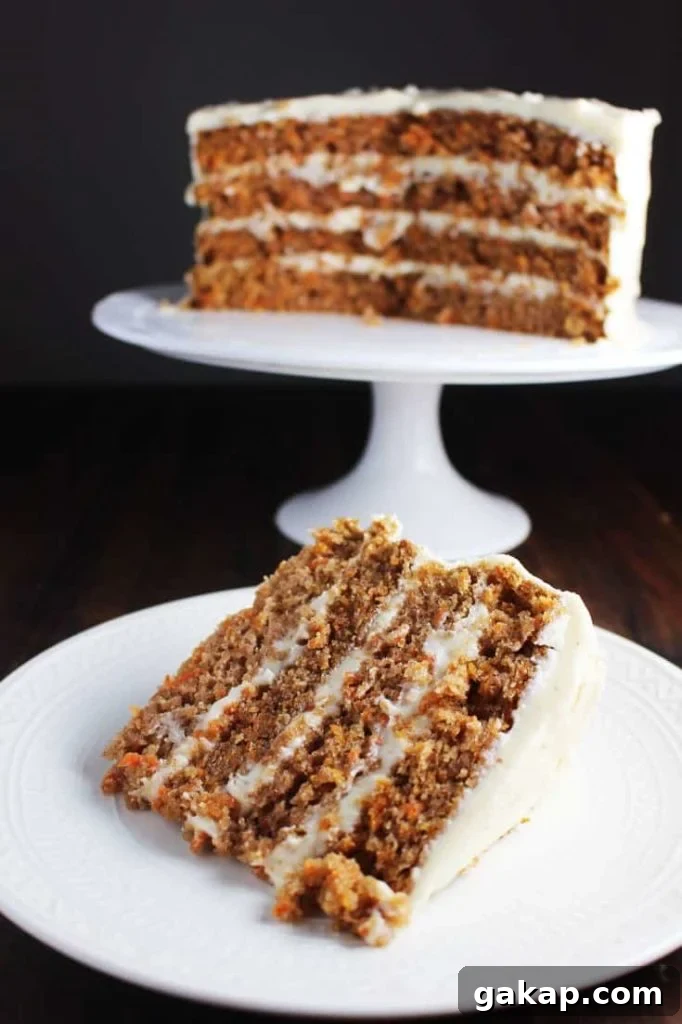 Slice of four layer moist carrot cake on a plate with cake on a stand in background.