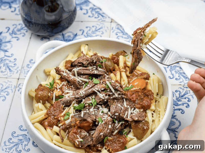 13 Classic Vintage Recipes for Cozy Fall Cooking 2 A white bowl of pasta topped with shredded beef, vegetables, and sauce sits on a patterned surface; a fork lifts some meat from the bowl.