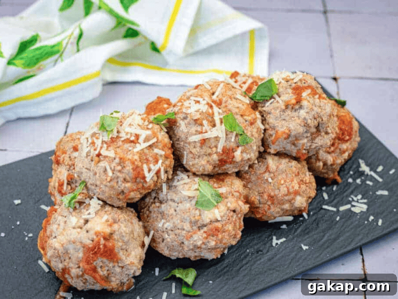 13 Classic Vintage Recipes for Cozy Fall Cooking 5 A stack of baked meatballs topped with grated cheese and fresh basil leaves on a black slate serving tray, with a white and yellow cloth in the background.