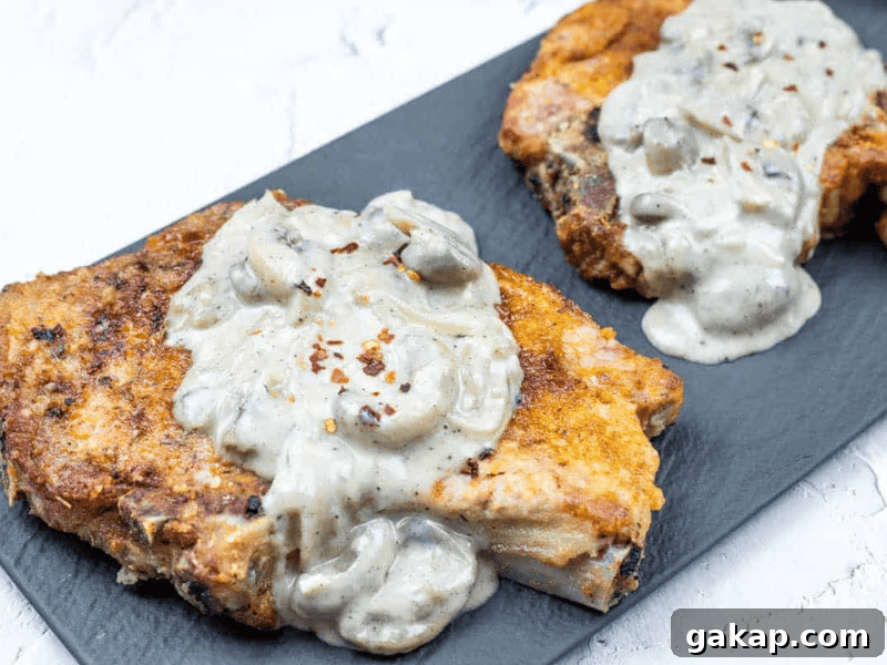 13 Classic Vintage Recipes for Cozy Fall Cooking 6 Two breaded pork chops topped with creamy mushroom sauce, served on a dark rectangular plate against a white background.