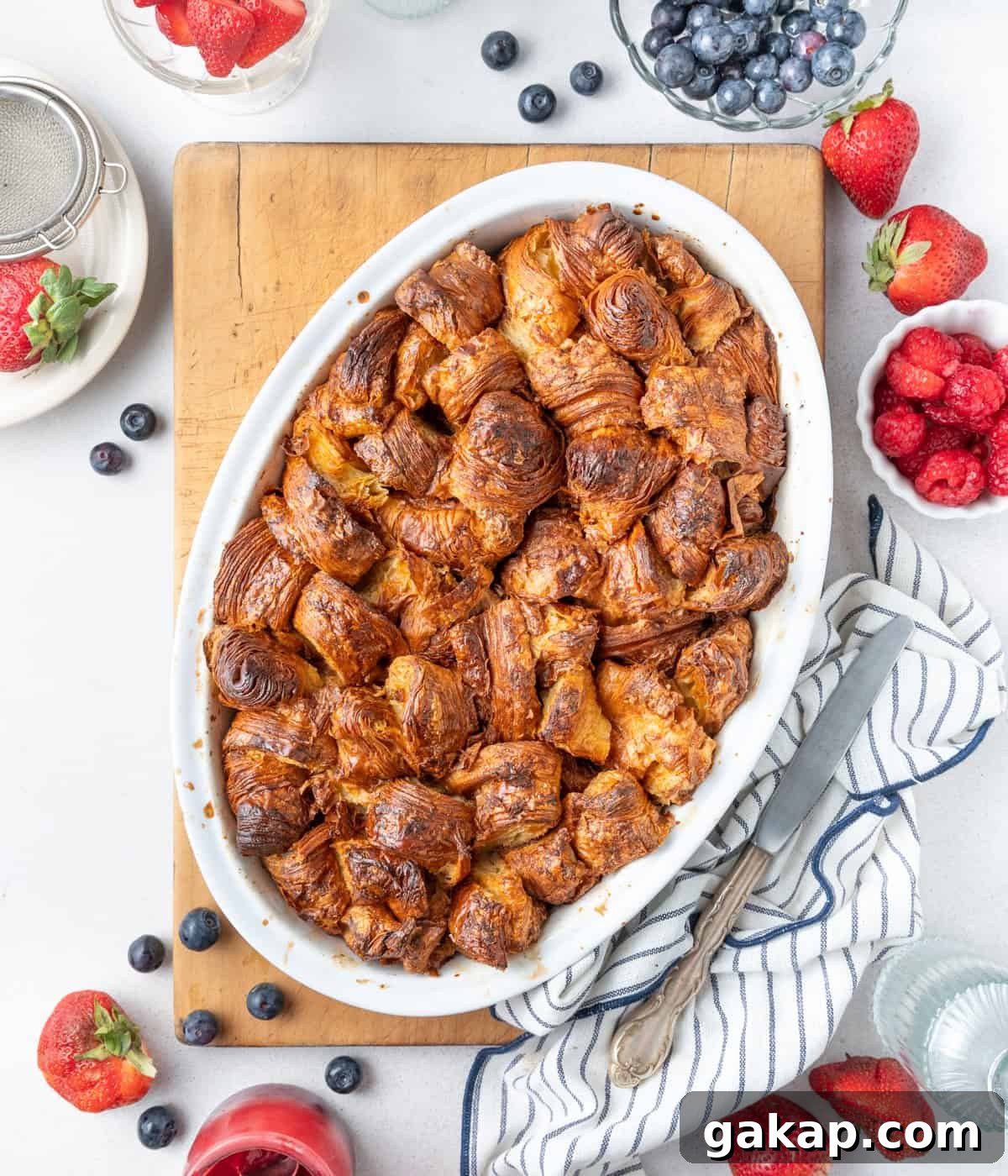 Decadent Croissant French Toast Casserole Recipe 5 Baked dish in an oval white ceramic dish placed on a large wooden cutting board.
