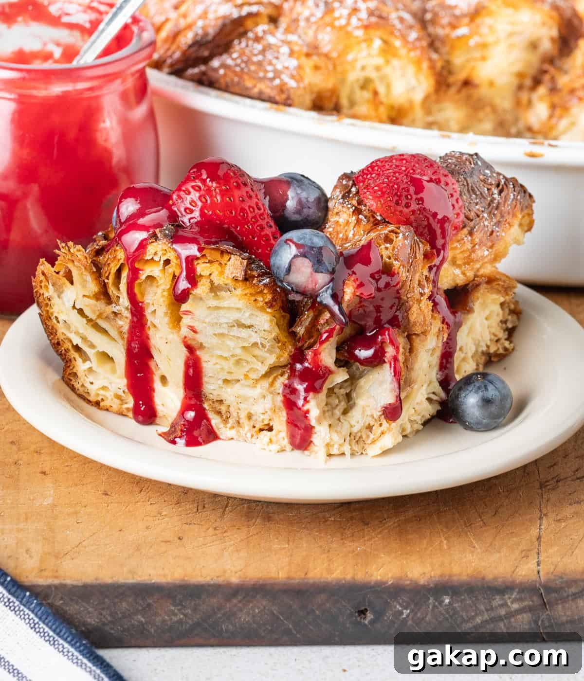 Decadent Croissant French Toast Casserole Recipe 6 Slice of french toast on a small plate topped with fresh berries and raspberry coulis drizzle.