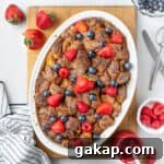 Decadent Croissant French Toast Casserole Recipe 10 French toast baked in a white oval dish seen from above, placed on a rectangular cutting board and topped with fresh berries.