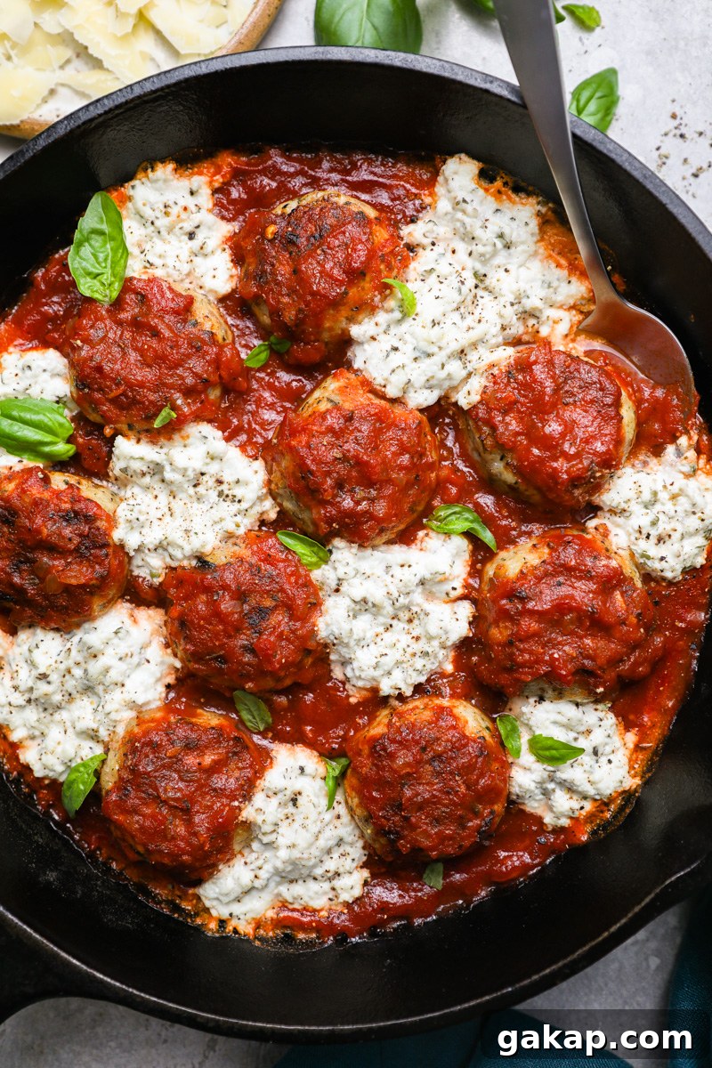 A large skillet filled with Italian chicken meatballs and herbed ricotta surrounded by fresh basil leaves and shredded parmesan
