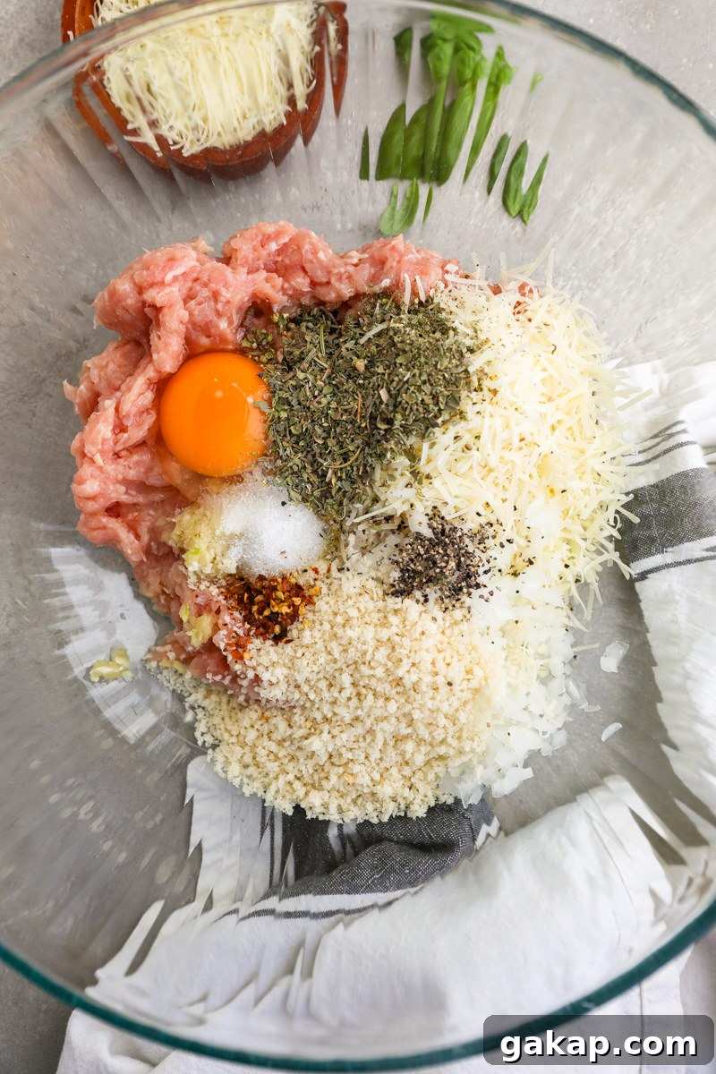 A large clear mixing bowl filled with the ingredients used to make Italian chicken meatballs