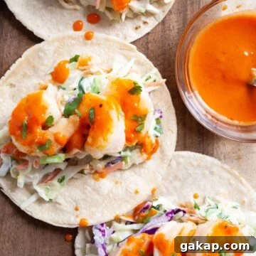 a close up view of bang bang shrimp tacos on a wooden board next to a bowl of bang bang sauce.