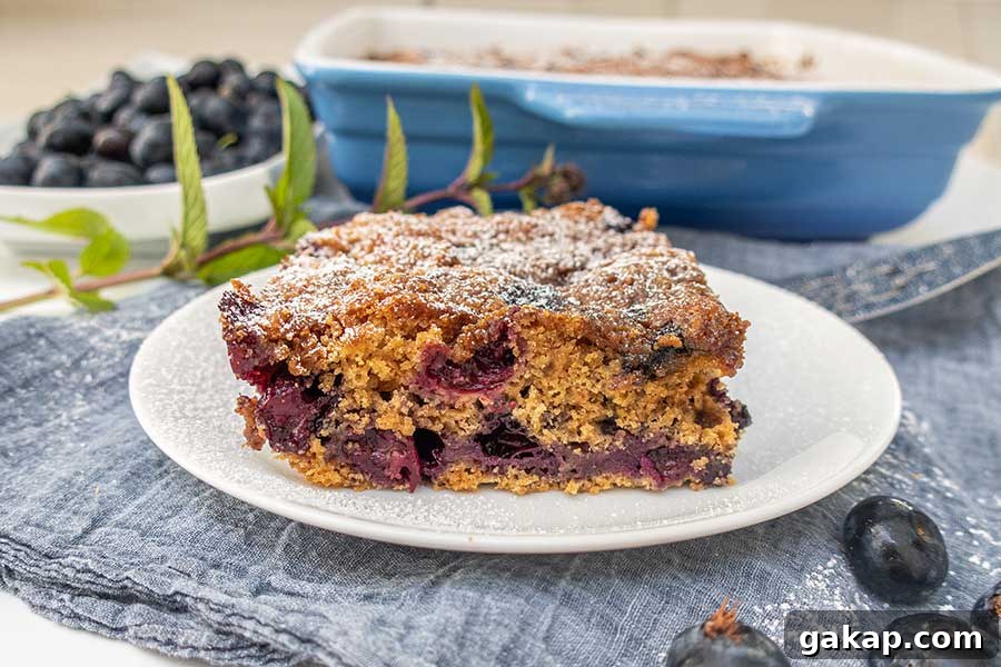 slice of buckle cake studded with blueberries and dusted with powdered sugar on a dessert plate