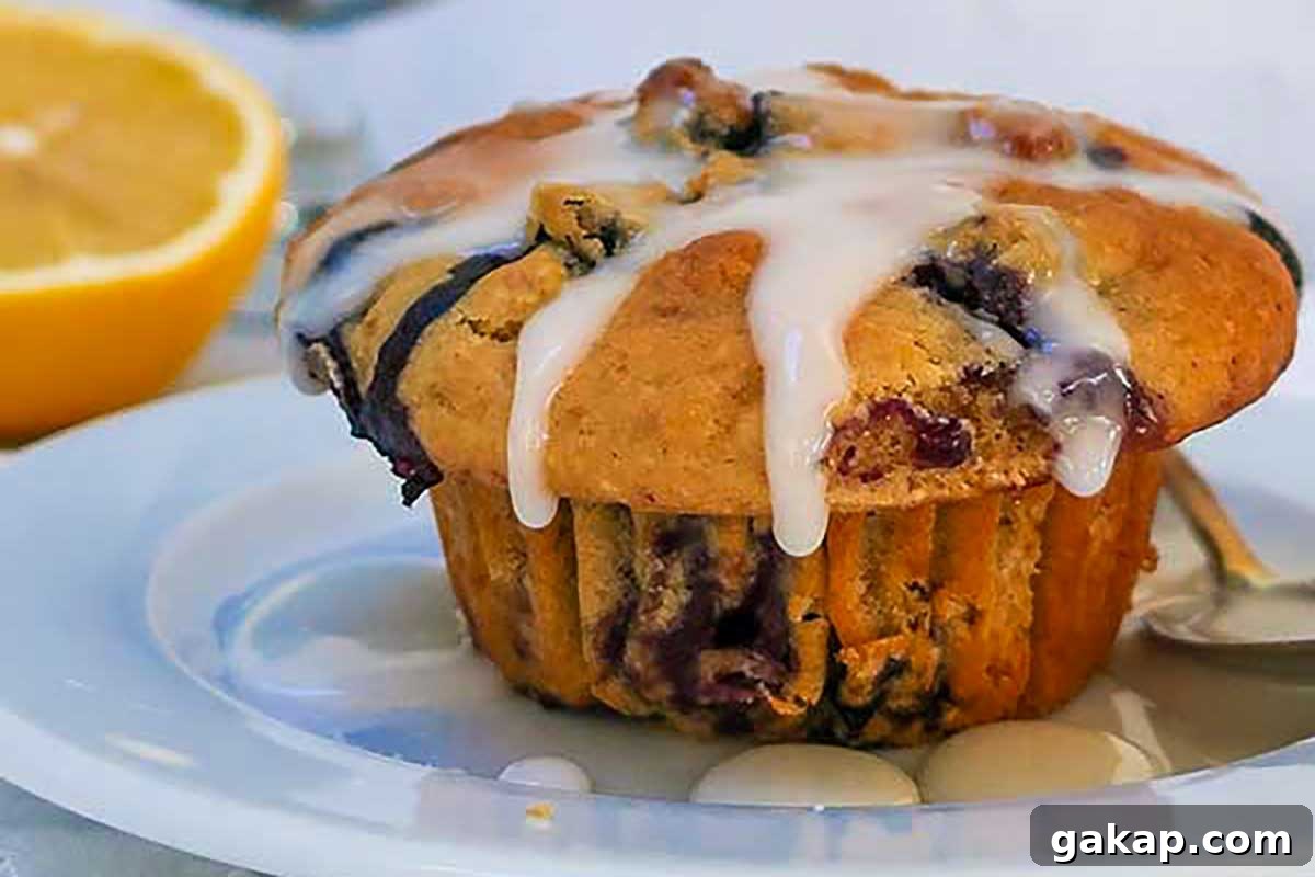 A light, fluffy muffin studded with juicy blueberries and drizzled with glossy lemon glaze, served on a plate—bright, fresh, and full of flavor