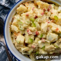 overhead shot of potato salad in a white bowl with a blue linen next to it.