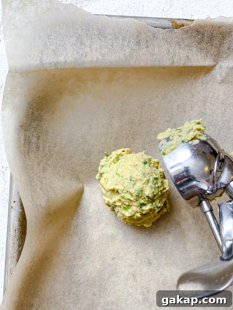 process shot of adding a scoop of baked falafel to baking sheet
