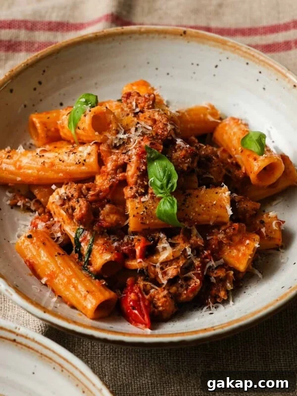 Creamy Roasted Red Pepper & Tomato Pasta Recipe 12 Pasta with sausage, cherry tomatoes, basil, and grated cheese in a ceramic bowl.