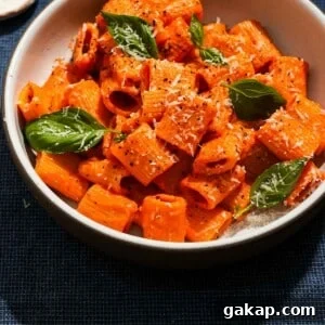 Creamy Roasted Red Pepper & Tomato Pasta Recipe 13 A large shallow bowl of roasted red pepper and tomato pasta with basil and parmesan cheese.