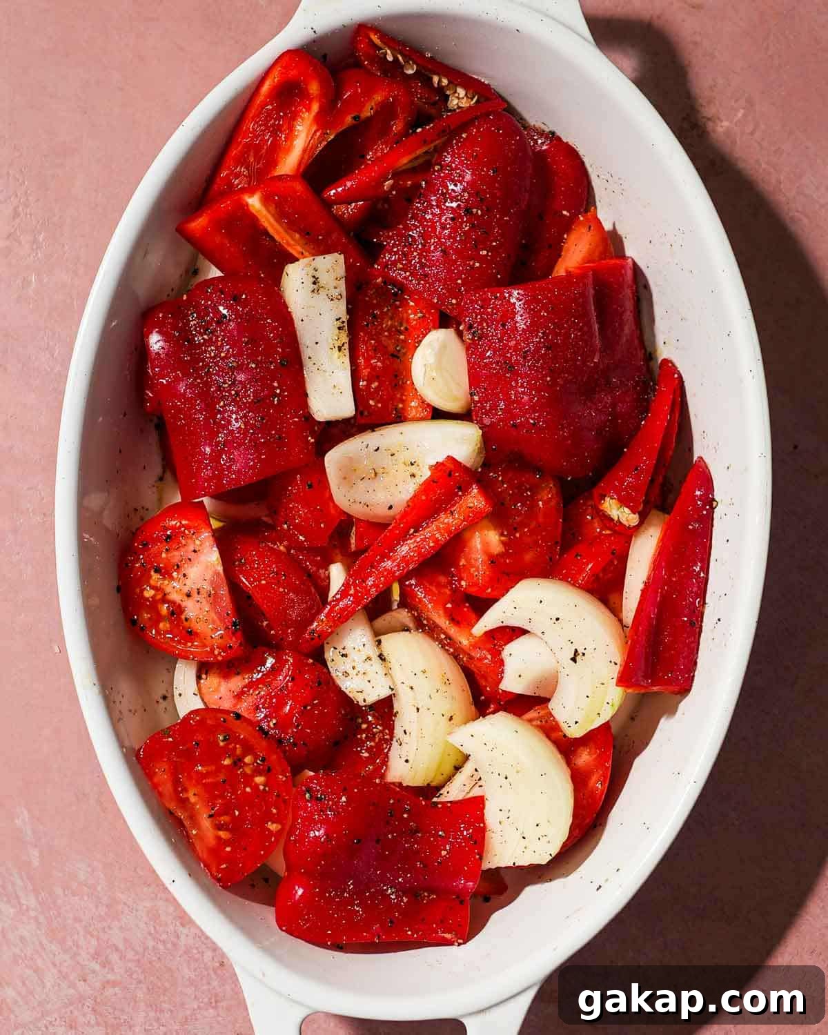 Creamy Roasted Red Pepper & Tomato Pasta Recipe 4 A white tray of red peppers, tomato, garlic, and onion ready to be roasted.