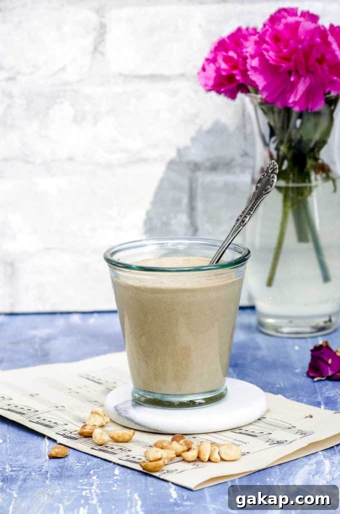 Side view of a glass cup with peanut sauce a a vase with flowers in the background