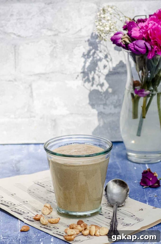 Side view of a glass cup with peanut sauce a a vase with flowers in the background