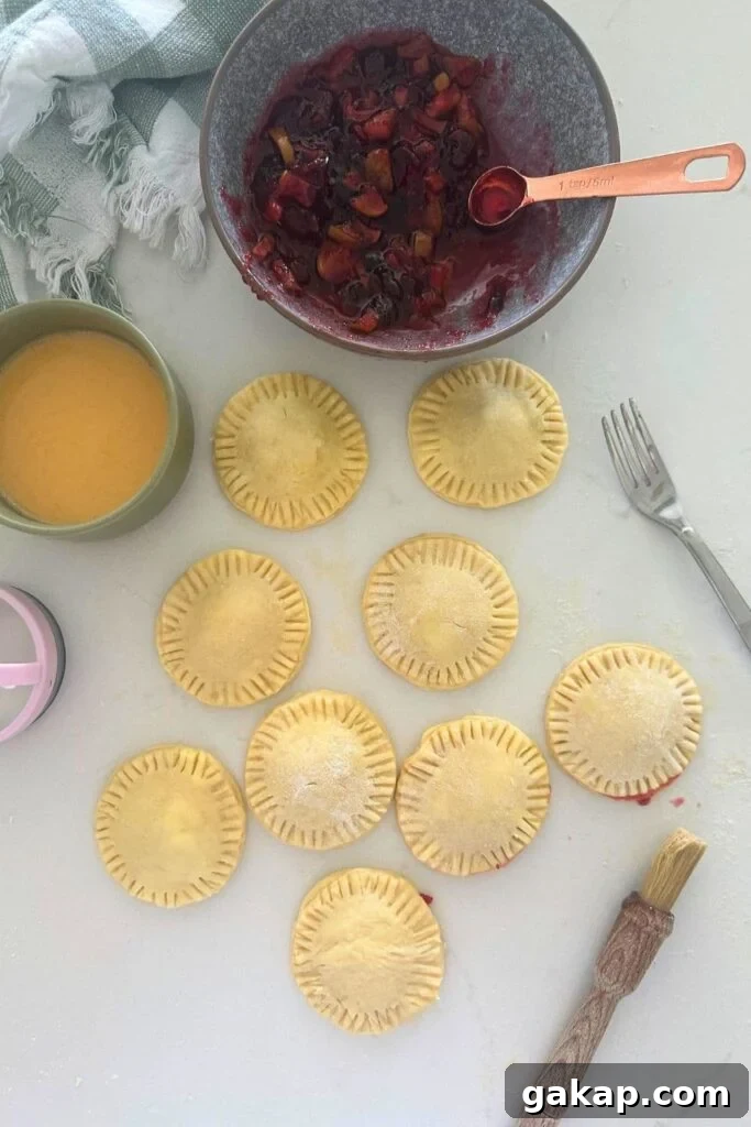 Apple Cranberry Sourdough Hand Pies Recipe for Flaky Pastries 3 A selection of sourdough hand pies that have been filled with apple and cranberry filling sitting on a white countertop. There is a bowl of apple and cranberry filling sitting near the pies.