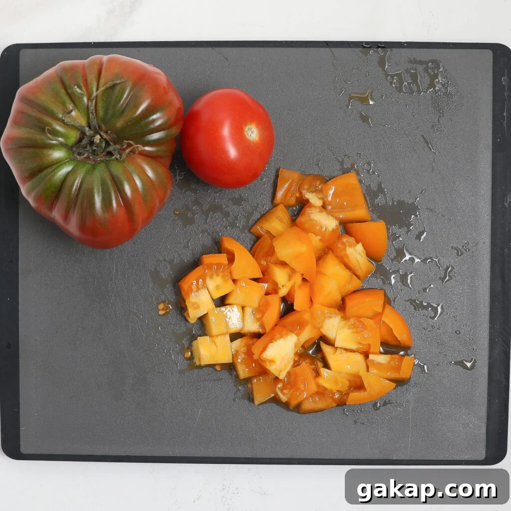 Tomato and Feta Bruschetta Recipe: Fresh Mediterranean Appetizer 3 Two whole tomatoes, one green and red, one red, rest on a gray cutting board next to chopped yellow tomato pieces—fresh ingredients perfect for a vibrant tomato feta bruschetta. The board is slightly wet with tomato juice.