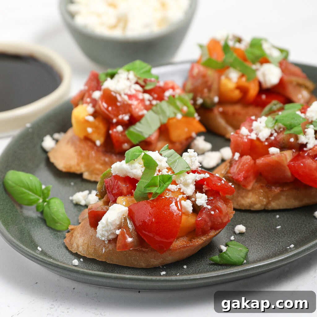 Tomato and Feta Bruschetta Recipe: Fresh Mediterranean Appetizer 5 A plate of tomato feta bruschetta topped with diced tomatoes, crumbled cheese, and fresh basil sits on a white surface. A bowl of balsamic vinegar and a small dish of cheese are in the background.