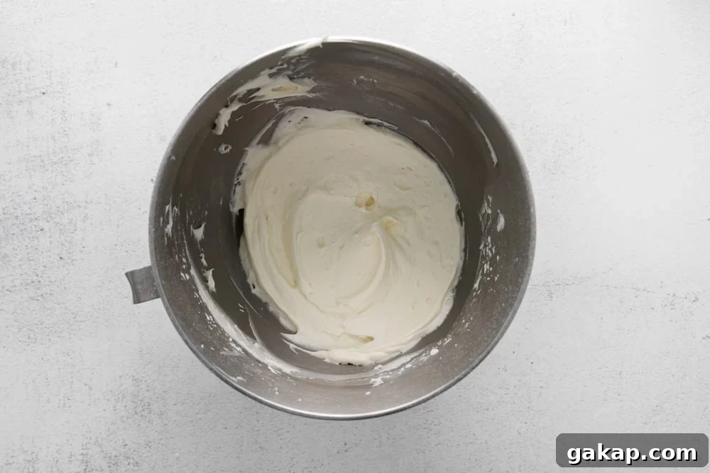Decadent Red Velvet Cupcakes with Cream Cheese Frosting 10 whipped cream in a metal mixing bowl on a white background.