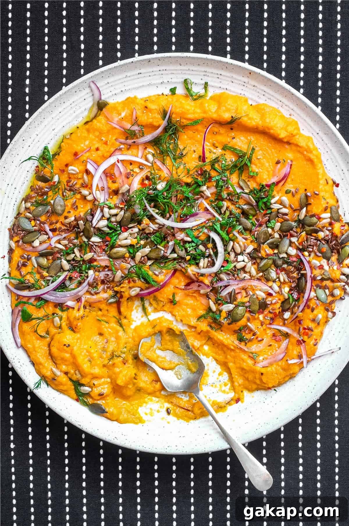 A platter of Turkish carrot salad scattered with herbs, seeds and red onion