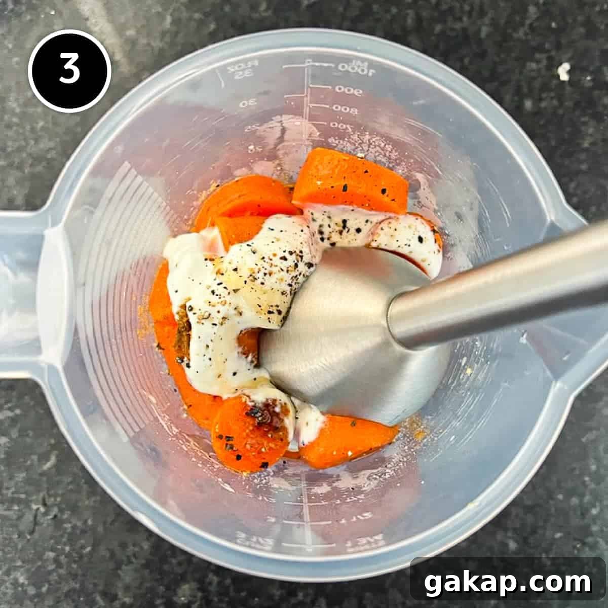 Carrots and yoghurt with spices in a plastic jug, about to be blended by a stick blender