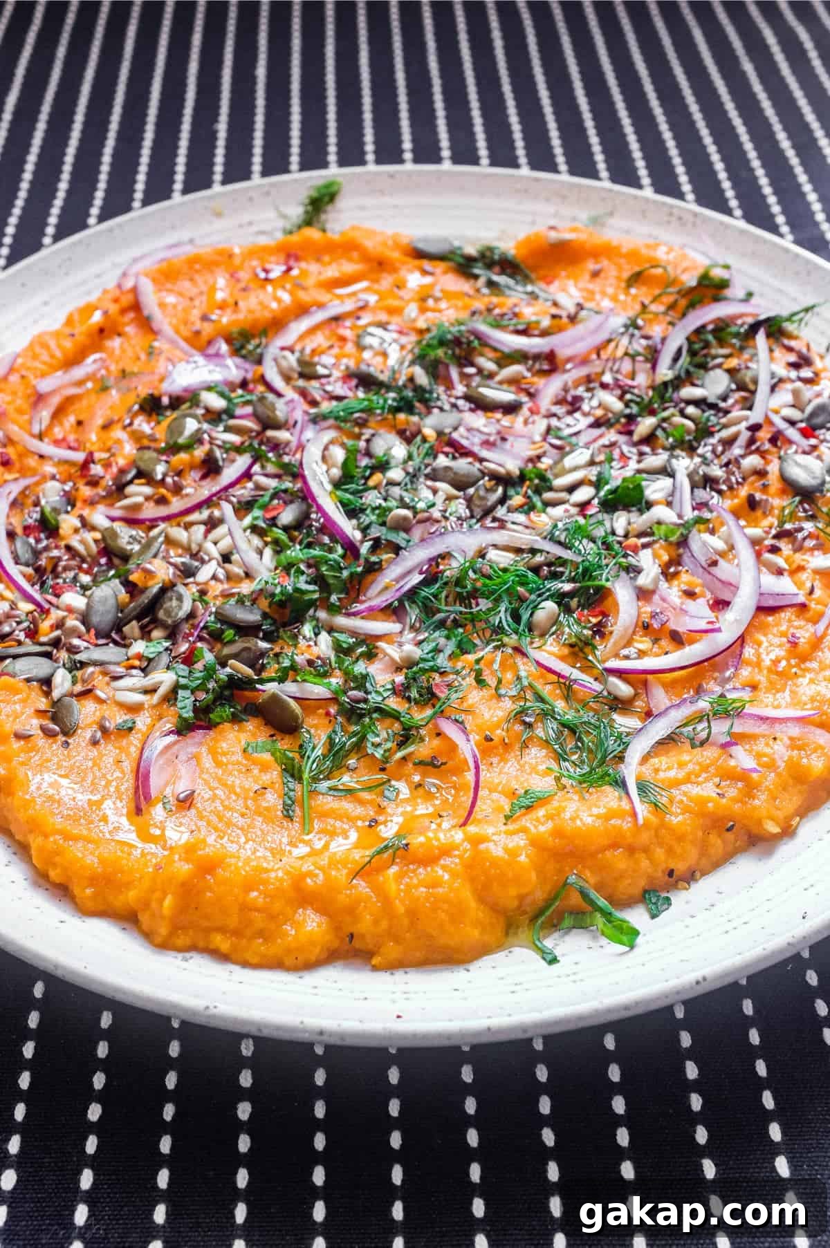 A platter of Turkish carrot salad scattered with herbs, seeds and red onion