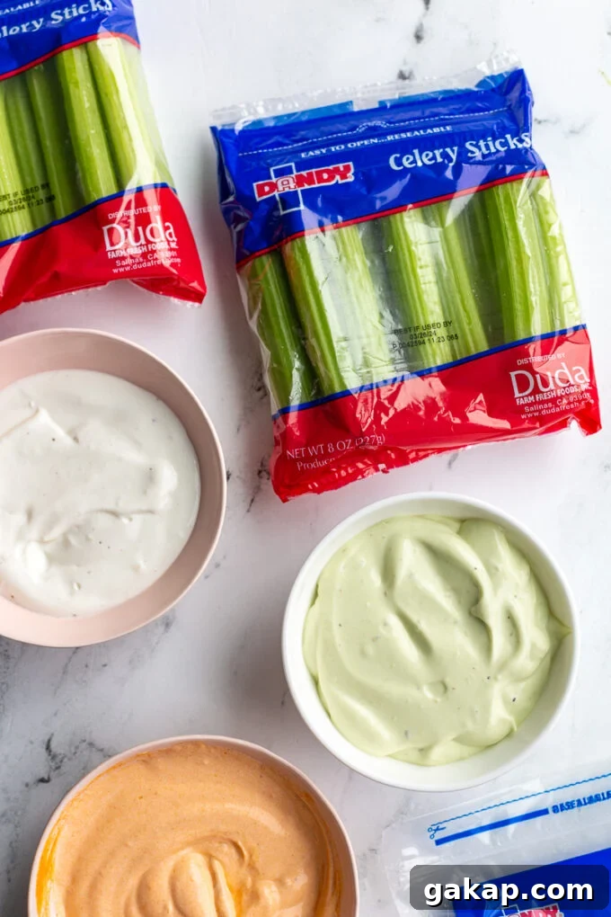 3 different flavors of whipped cottage cheese in 3 different bowls: plain, avocado, and buffalo flavors. There are small bags of Dandy fresh celery in the corner of the shot