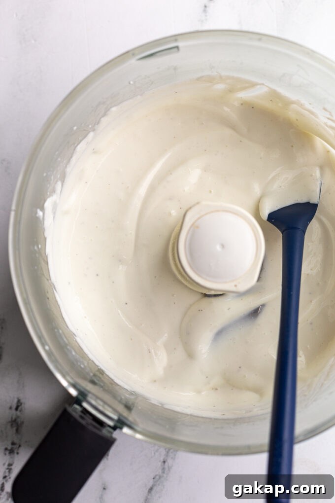whipped cottage cheese in a food processor with the top off and a navy blue spatula hanging out the side