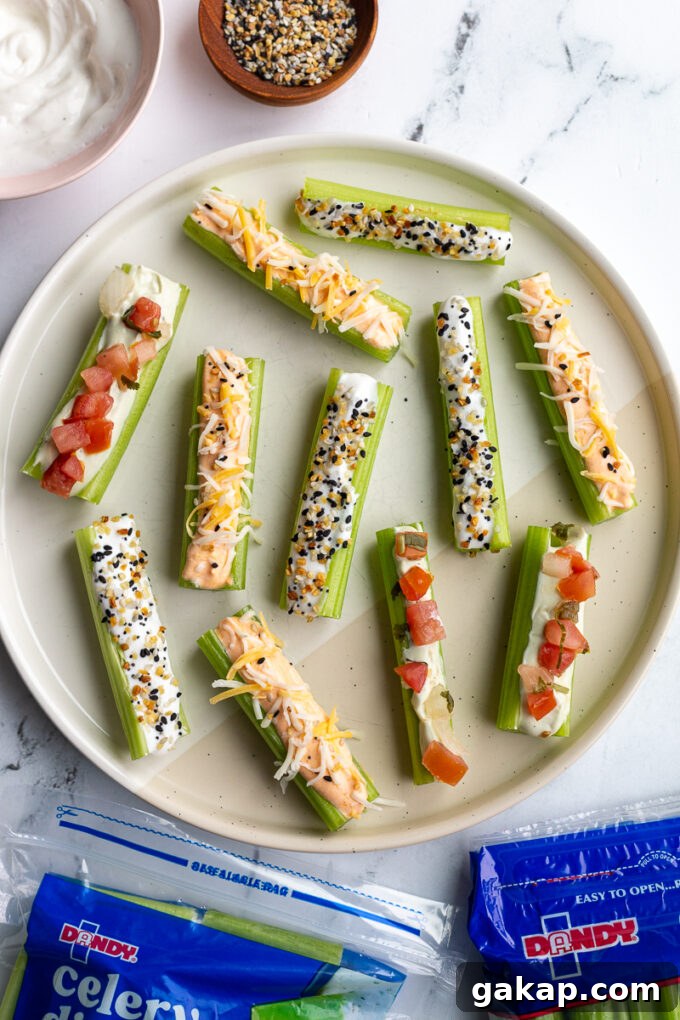 celery sticks on a white plate flavored 3 different ways: whipped buffalo cottage cheese topped with shredded cheese, whipped cottage cheese topped with everything but the bagel seasoning, and whipped avocado cottage cheese topped with pico de gallo. bags of dandy fresh celery in the corner of the shot