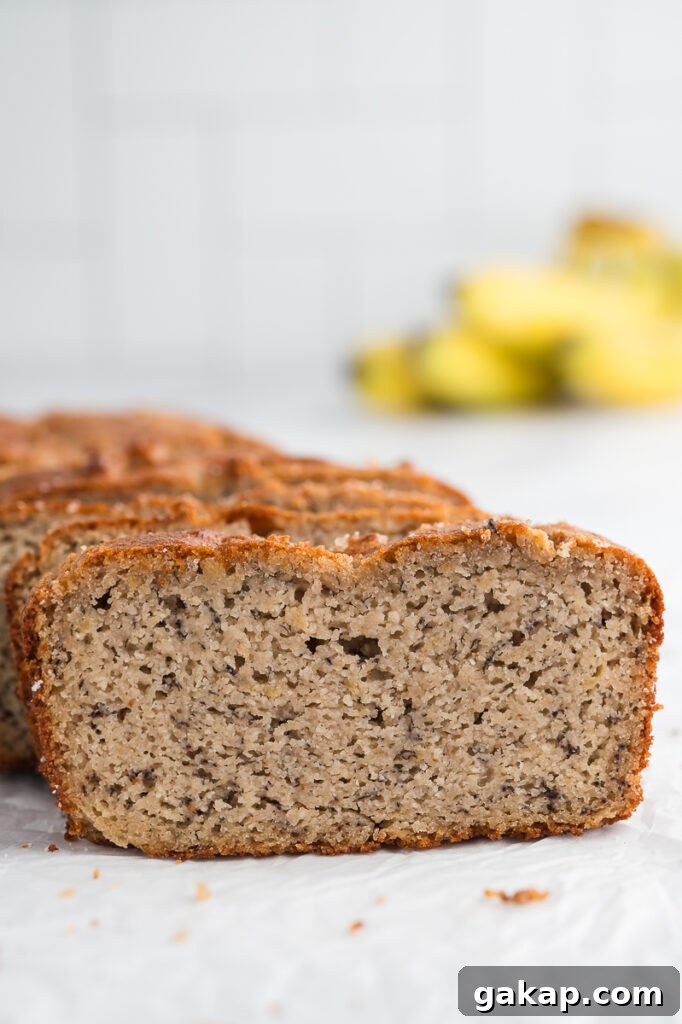 Sliced almond flour banana bread loaf showing soft moist crumb with ripe bananas in the background.